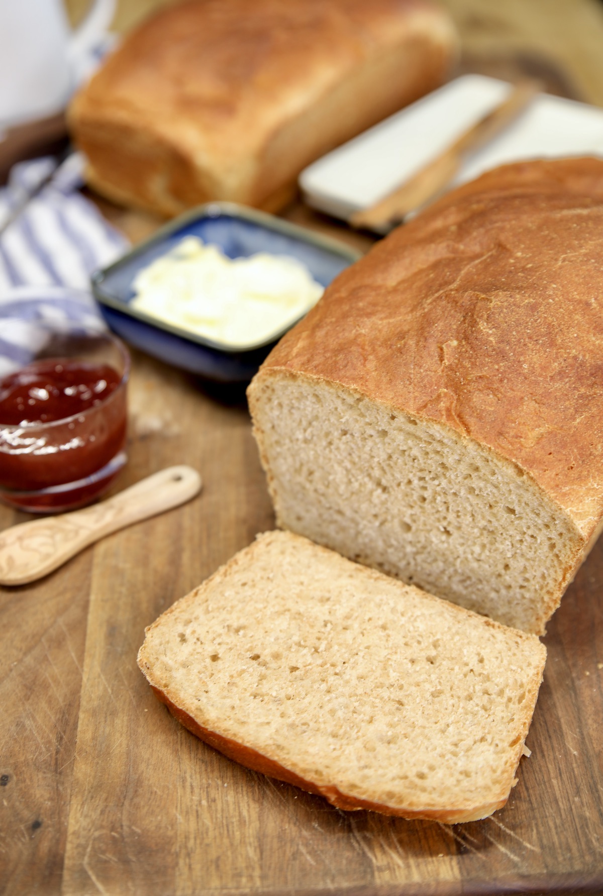 Loaf of bread partially sliced with butter and jam to the side.