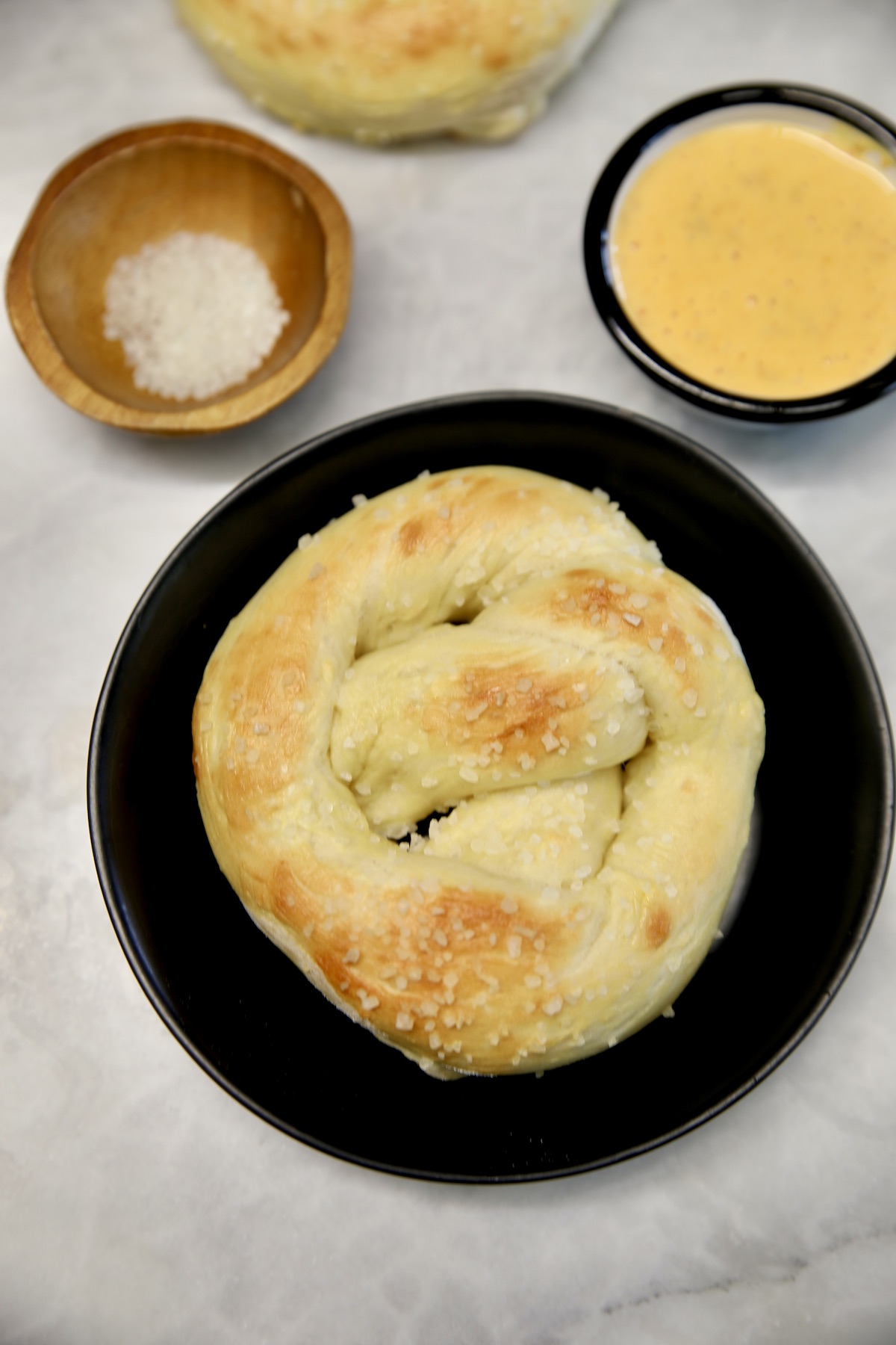 Soft pretzel in a bowl with bowl of salt and bowl of cheese sauce.