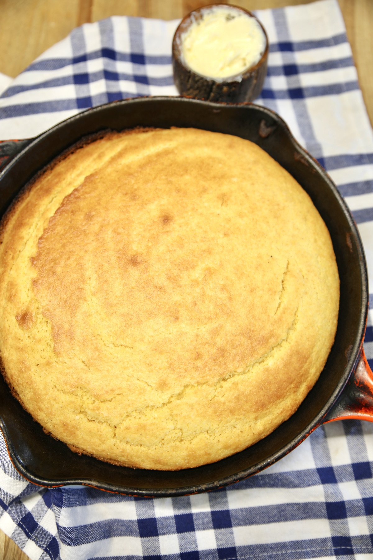 Skillet of cornbread on a blue and white towel, bowl of butter.