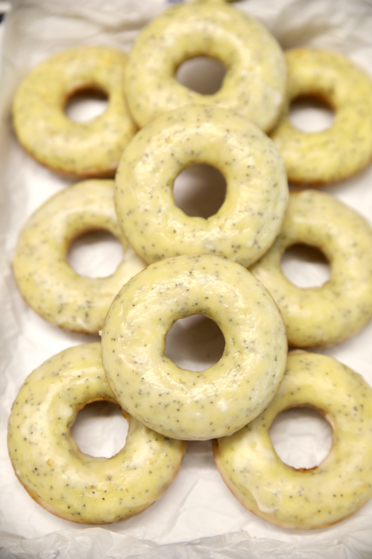 Glazed lemon poppy seed donuts stacked on a pan.