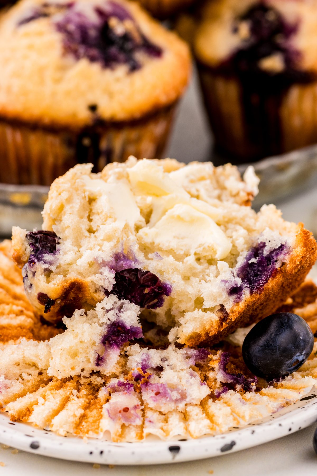 Open face blueberry muffin smeared with butter. Fresh blueberry muffin open with butter and blueberries.