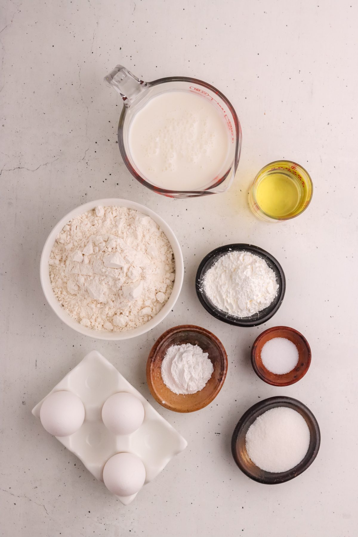 Waffle ingredients. Milk, lemon juice, flour, sugar, eggs, salt, and oil in individual bowls.
