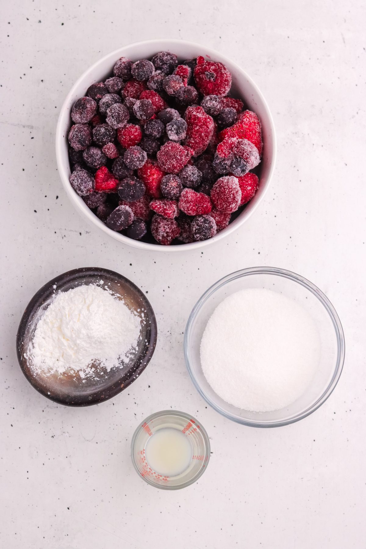 Mixed berry compote ingredients. Frozen mixed berries, cornstarch, lemon juice, and sugar in individual bowls.
