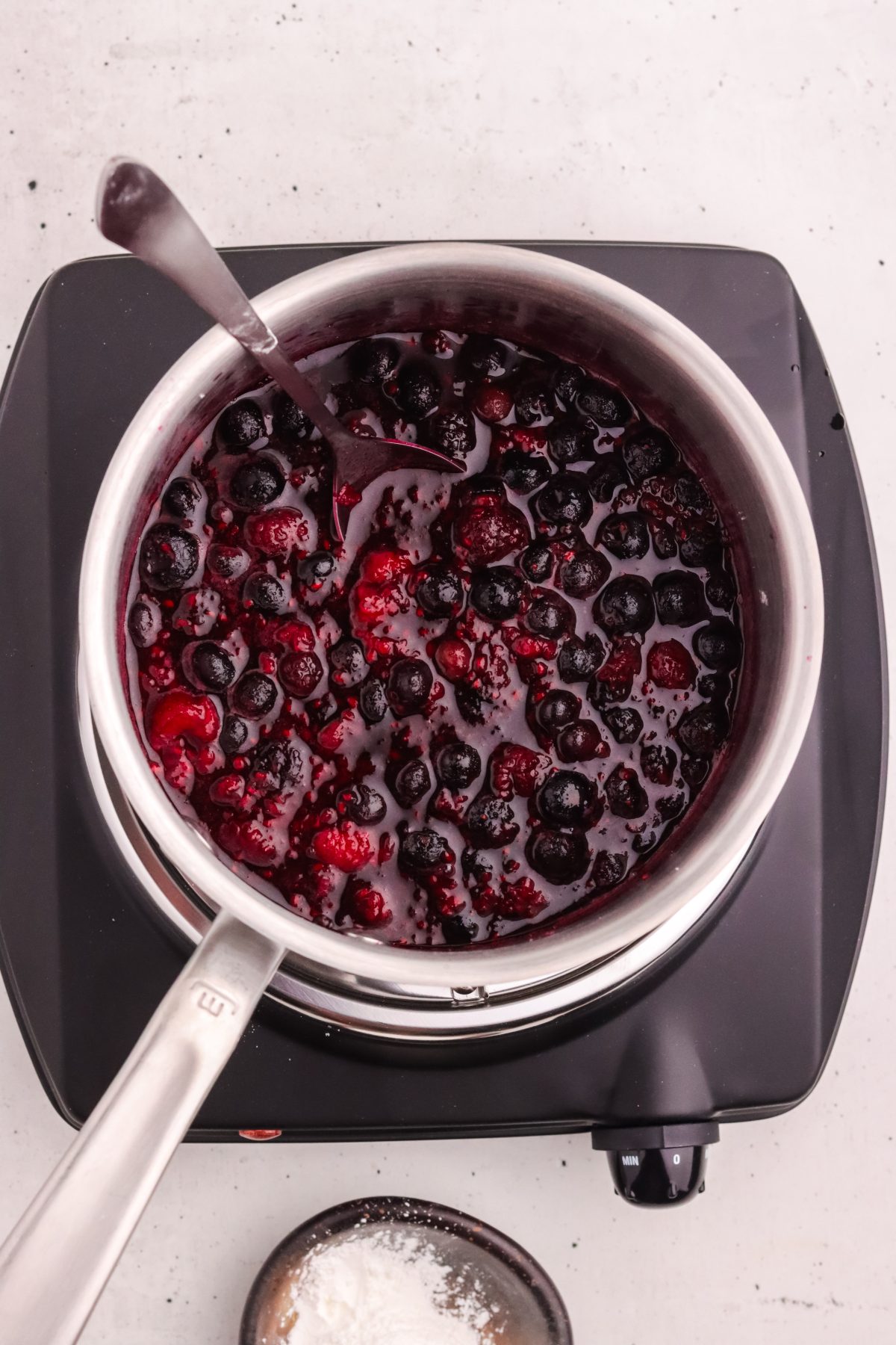 Mixed berry compote cooking on a heat plate. Mixed berry compote on a stainless steel pot on a warming plate.