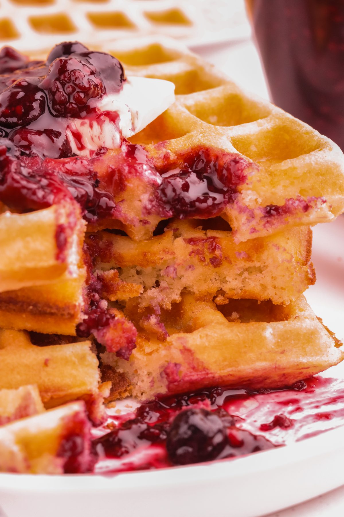 Fresh crispy waffles with mixed berry compote. 3 stacked waffles with butter and berry compote on a white plate.