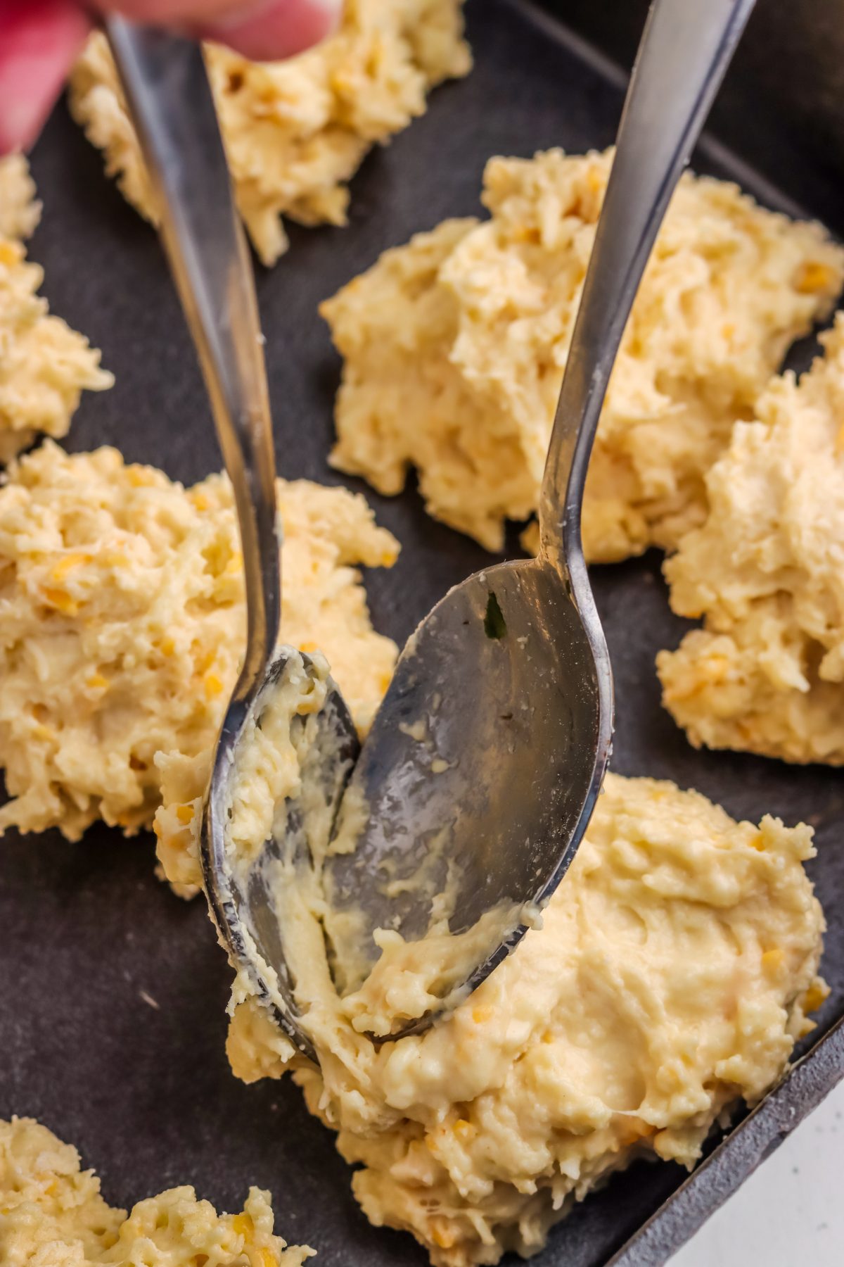 garlic cheese biscuit dough being spooned onto a baking sheet drop biscuit dough being spooned onto a baking sheet.