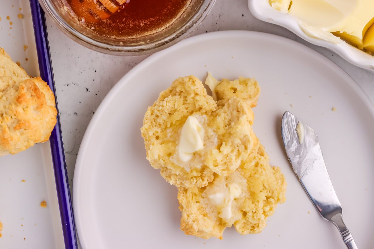 Fresh baked drop biscuit with butter spread. Baked drop biscuit cut in half with spread butter on white plate.