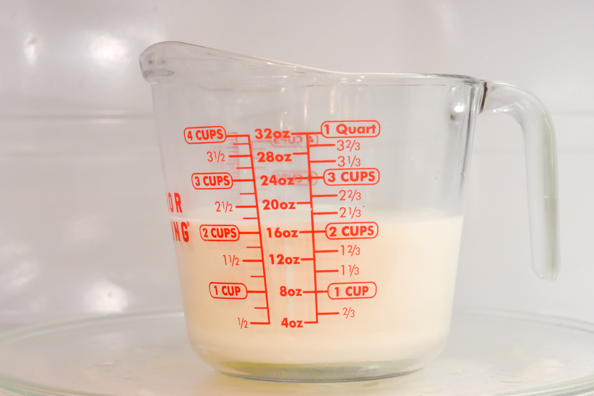 Two cups of milk in a measuring cup in the microwave.
