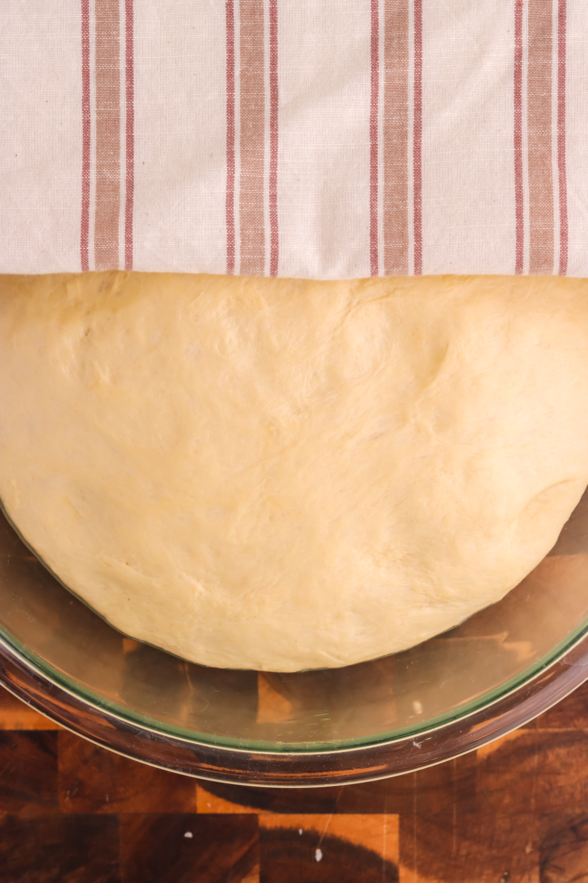 Soft pretzel dough rising in a glass bowl with a towel covering.