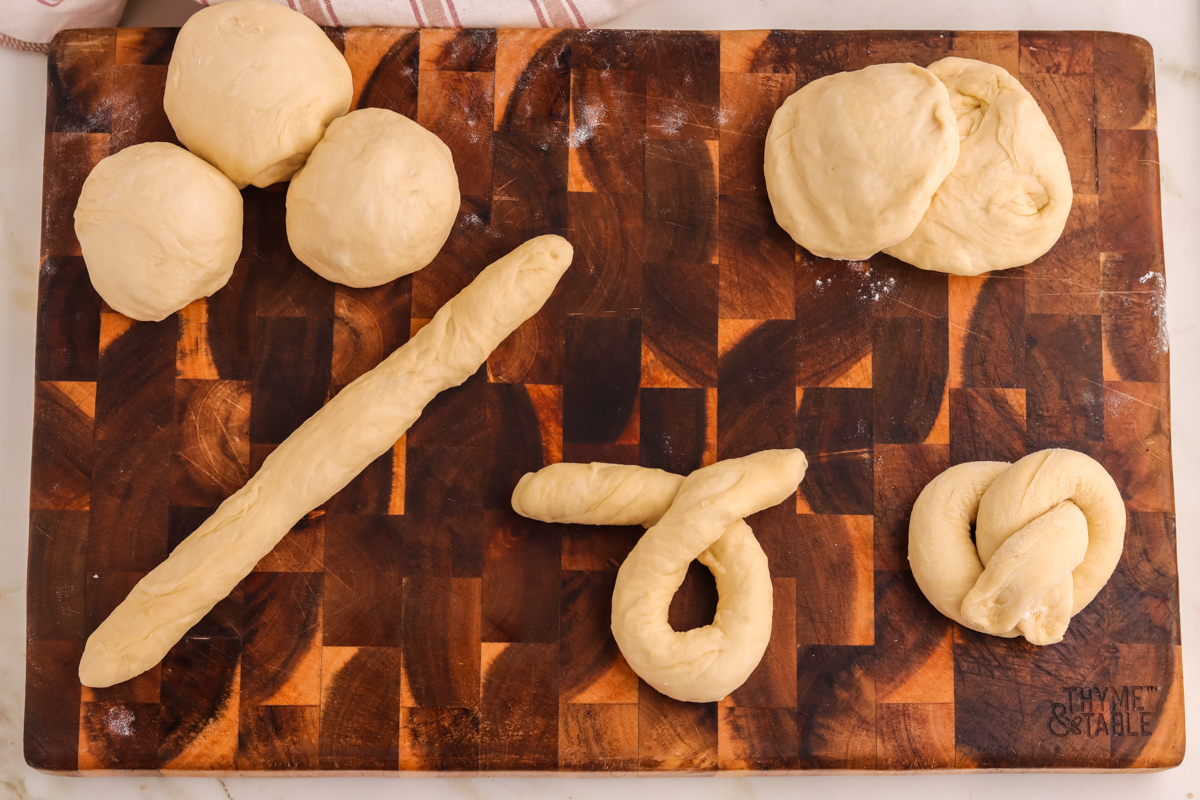 Pretzel dough balls, rolled into shaped to from pretzels on a wood board.