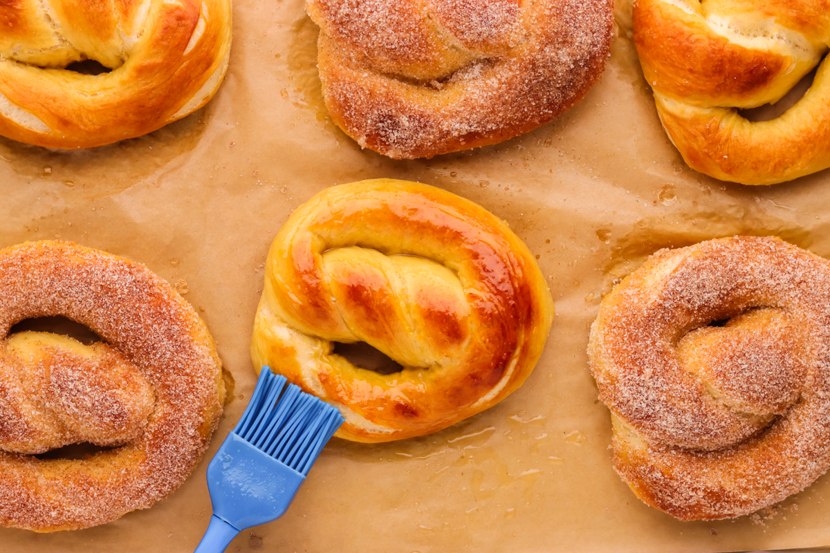 Pretzels on a parchment lined baking sheet coated in butter and cinnamon sugar. 
