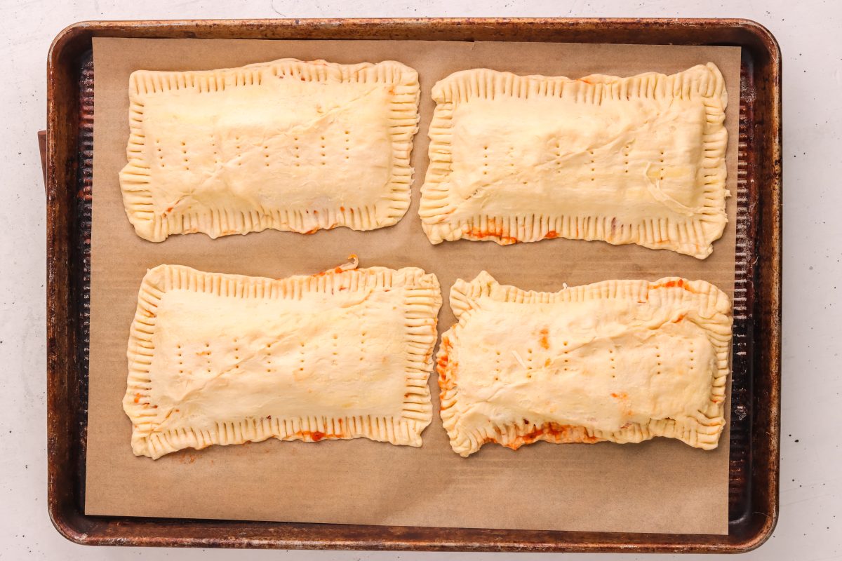 Filled pizza pockets on a lined baking sheet. Filled pizza pockets on a lined baking sheet.